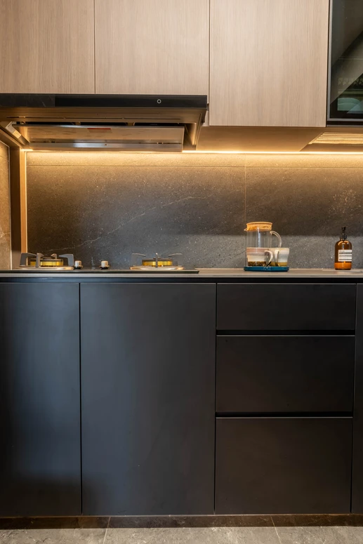 Compact kitchen design featuring black lower cabinets, wood-finished upper units, and a stone backsplash.