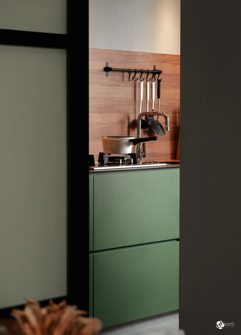 Compact kitchen featuring matte green cabinet design and a warm wooden backsplash.